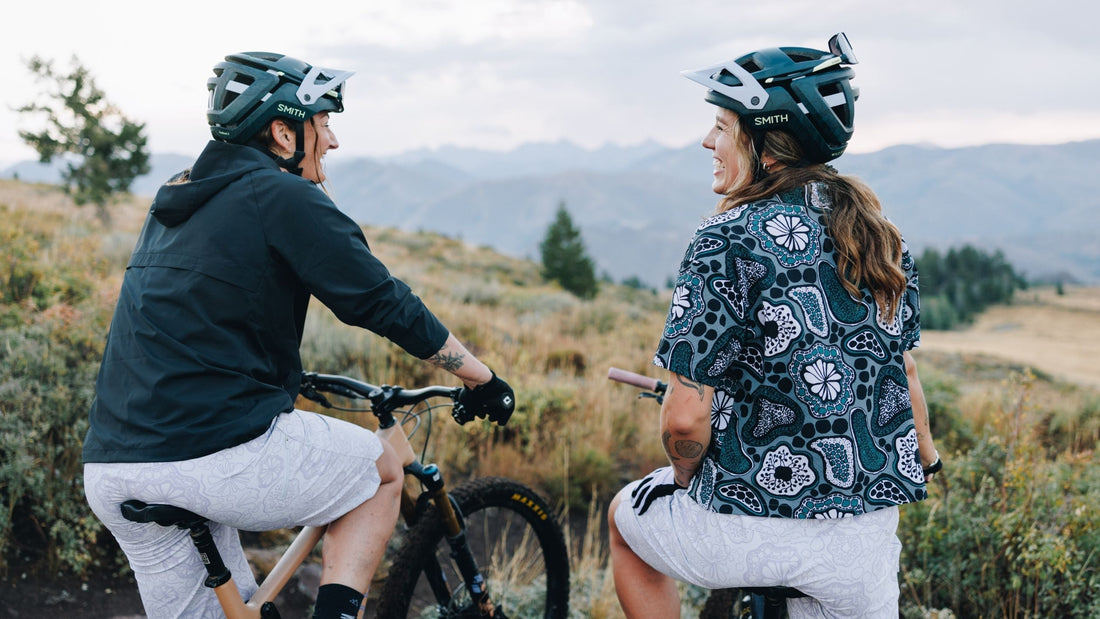 Two women on bikes both wearing the Smith x Wild Rye collaboration collection. 