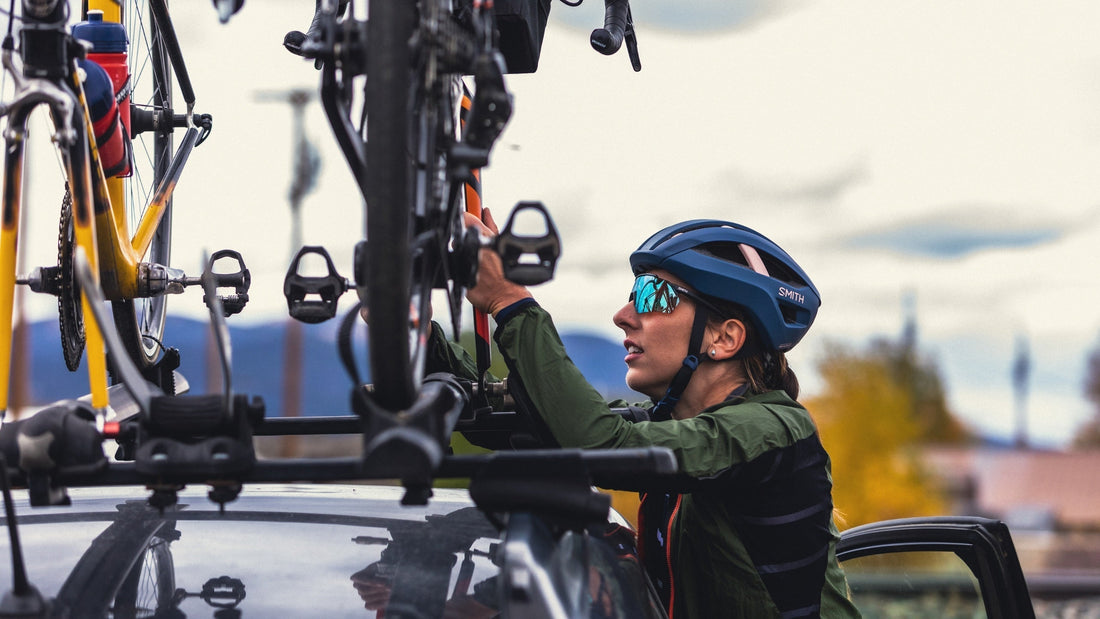 Woman wearing a Smith helmet and sunglasses reaches up to adjust the bike rack on the top of her car. 