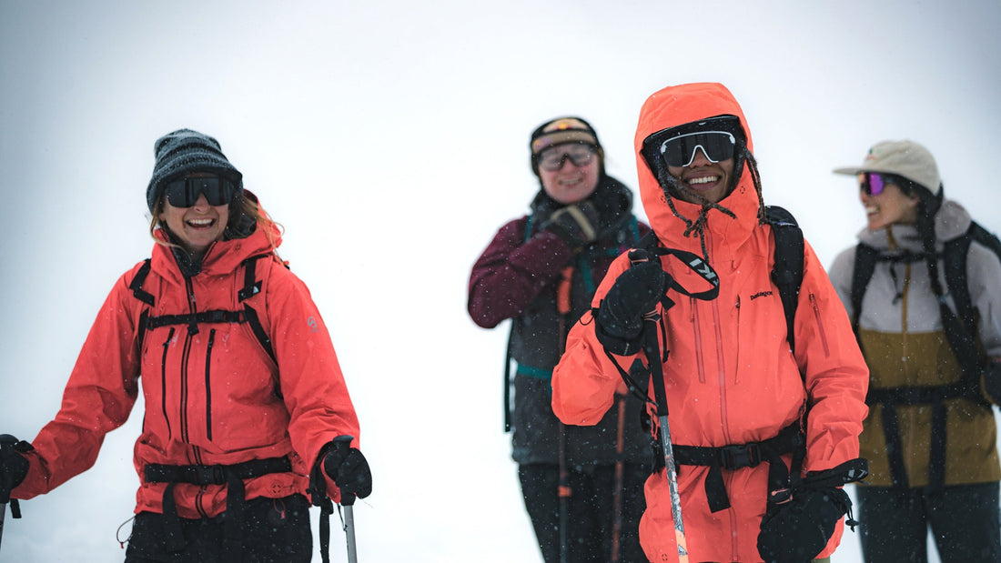 Four women hiking in the snowy backcounty, wearing winter clothes and sunglasses. 