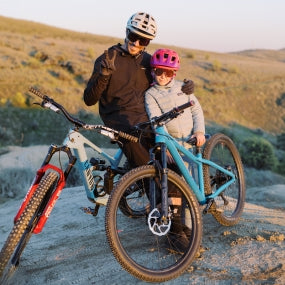 A man and a child wearing Smith bike helmets smile for the camera while out for a mountain bike ride.