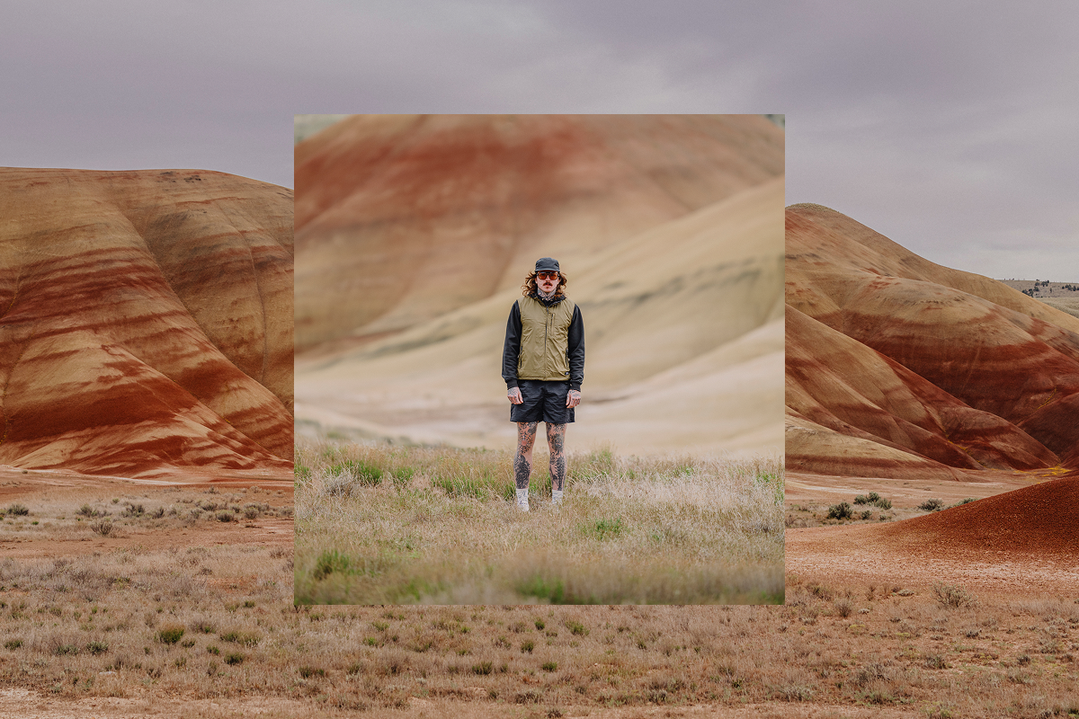 A man stands in a patch of dry grass in a desert landscape.