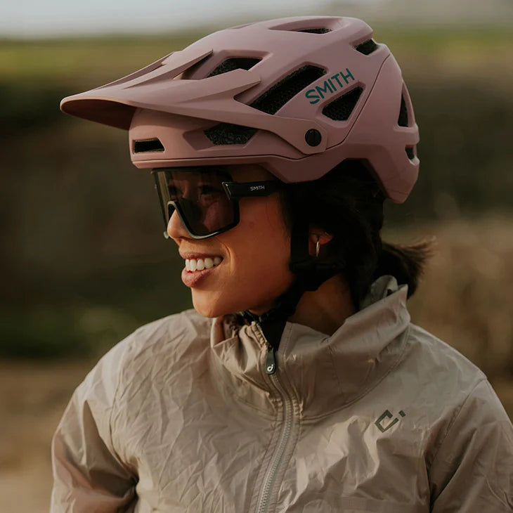 Person wearing a pink Smith helmet and sunglasses with a blurred natural background
