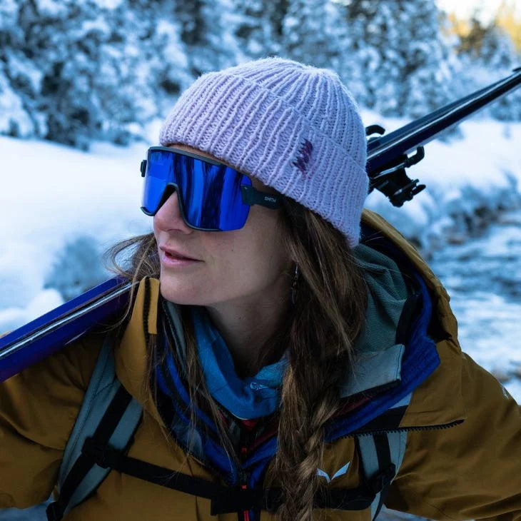 Person wearing a beanie and goggles with skis on a snowy background