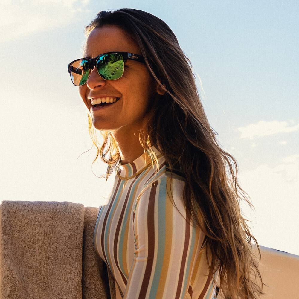 Woman smiling wearing sunglasses carrying a surfboard Woman smiling wearing sunglasses carrying a surfboard